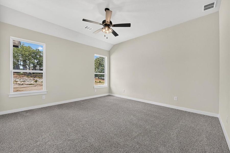 Spacious room featuring vaulted ceilings, two large windows, a ceiling fan with integrated lighting, neutral wall tones, and plush carpeting Spacious room featuring vaulted ceilings, two large windows, a ceiling fan with integrated lighting, neutral wall tones, and plush carpeting