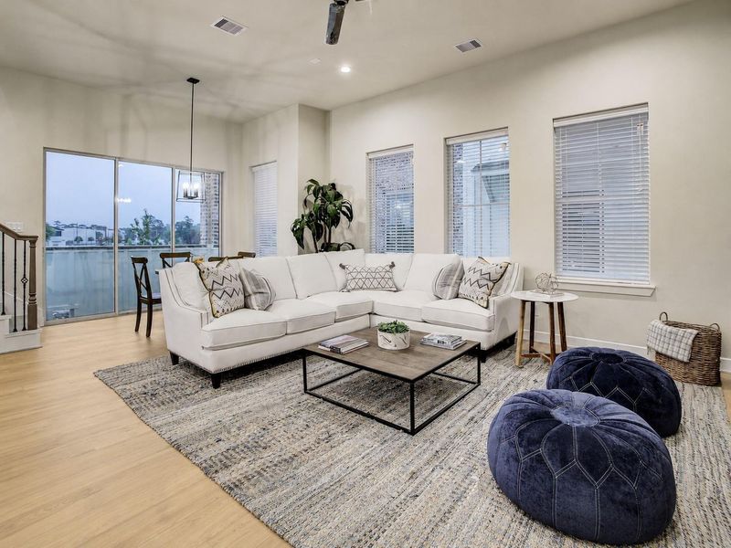 Sun-drenched living room — plush sectional seating arrangement framed by classic window blinds, soft warm wood flooring, and direct balcony access. Sun-drenched living room — plush sectional seating arrangement framed by classic window blinds, soft warm wood flooring, and direct balcony access.