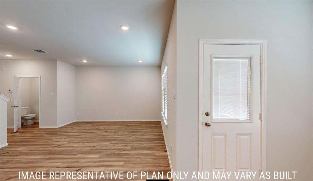 Open-concept interior featuring wood-finish flooring, recessed lighting, and a white paneled door with integrated blinds