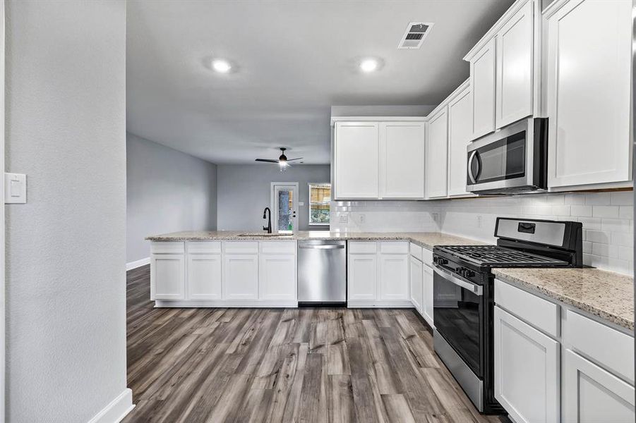 Kitchen with stainless steel appliances, a sink, wood finished floors, visible vents, and backsplash