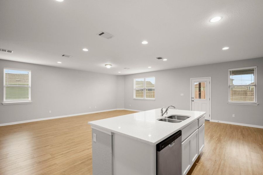Kitchen with stainless steel dishwasher, light wood finished floors, a center island with sink, white cabinets, and light countertops