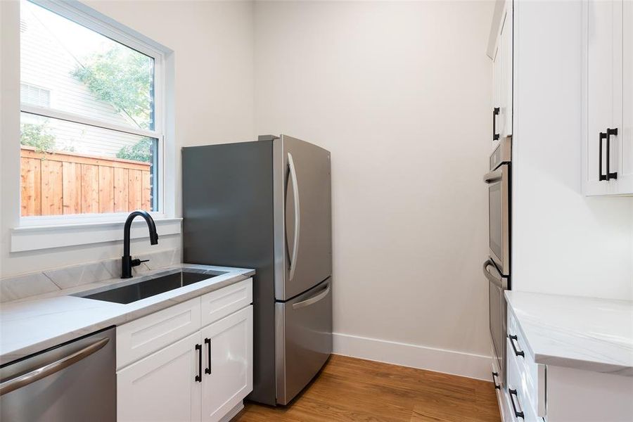 Kitchen featuring sink, light stone counters, light hardwood / wood-style floors, stainless steel appliances, and white cabinets