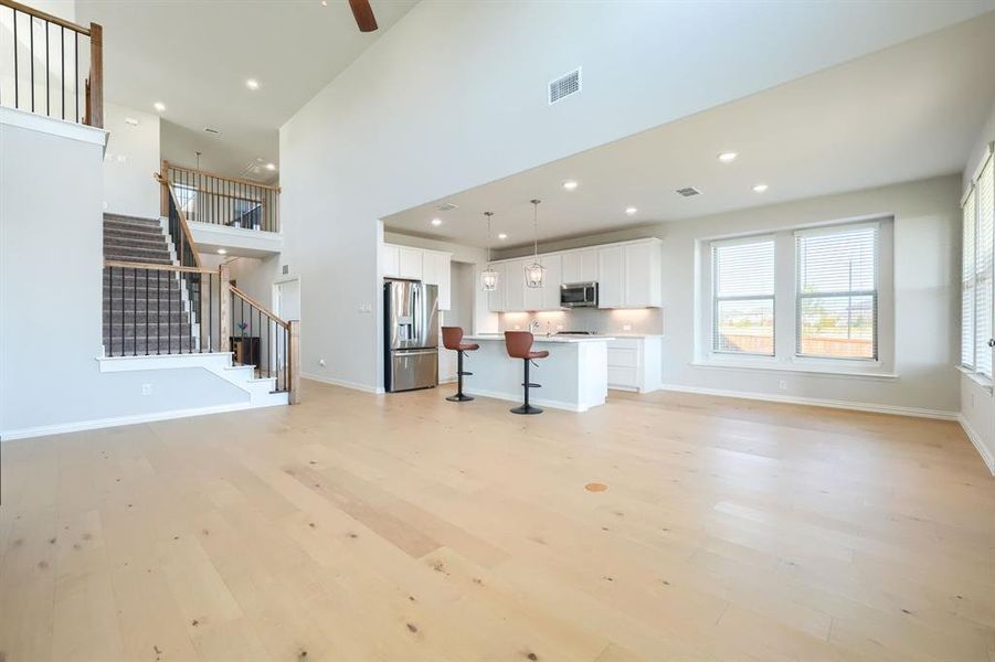 Unfurnished living room with light wood-type flooring, stairs, recessed lighting, a towering ceiling, and a ceiling fan Unfurnished living room with light wood-type flooring, stairs, recessed lighting, a towering ceiling, and a ceiling fan