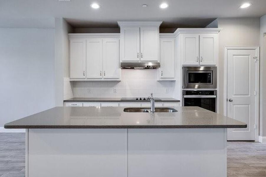 Kitchen featuring appliances with stainless steel finishes, a sink, white cabinets, a kitchen island with sink, and backsplash