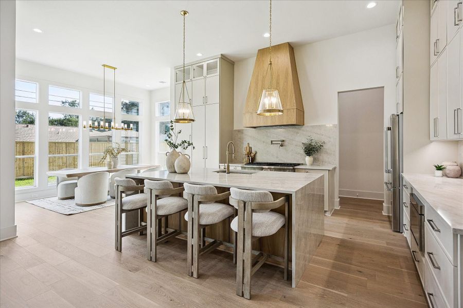 This is the kind of kitchen that makes everyday life feel special, with Taj Mahal countertops and a full slab backsplash, floor to ceiling cabinetry, and an oversized waterfall island that naturally draws everyone together.