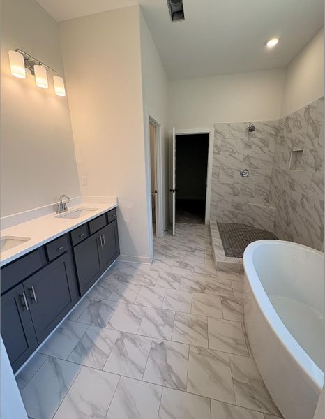 Bathroom featuring a soaking tub, double vanity, walk in shower, light marble finish flooring, and recessed lighting