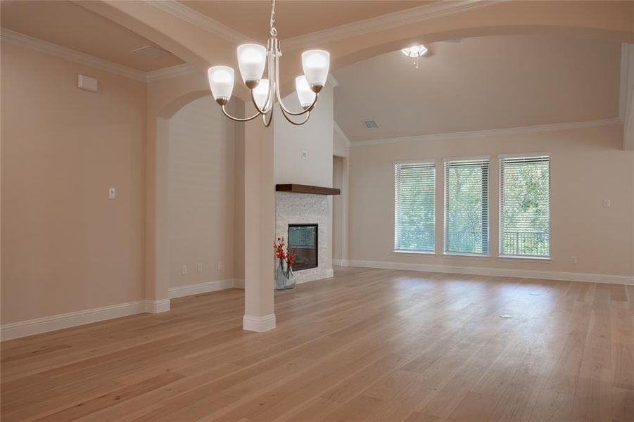 Unfurnished living room featuring light wood-type flooring, a stone fireplace, lofted ceiling, crown molding, and an inviting chandelier