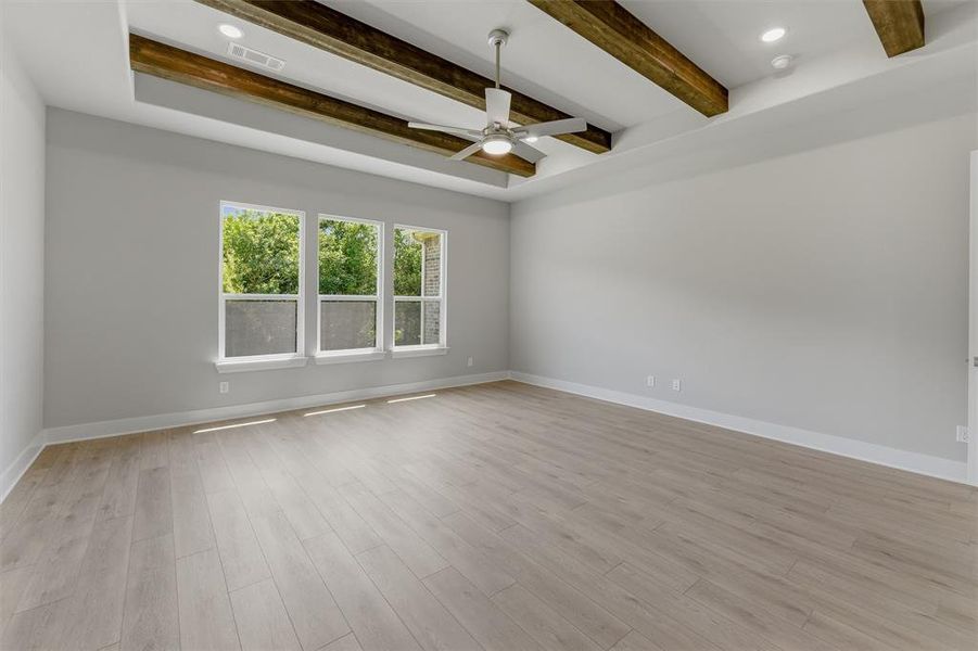 Spacious interior room featuring wood-finish flooring, a tray ceiling with exposed wood beams, and a ceiling fan with integrated lighting