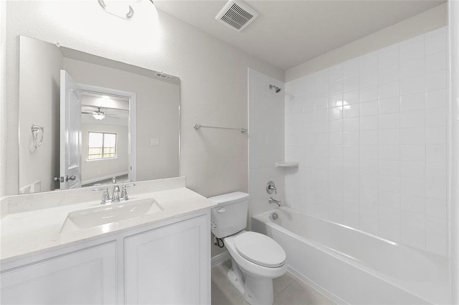 Full bathroom with tile flooring, ceiling fan, vanity with extensive cabinet space, tiled shower / bath, and toilet