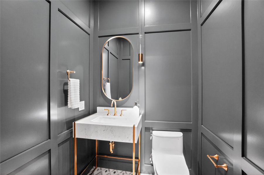 A striking powder room features a chic marble vanity and polished gold fixtures.