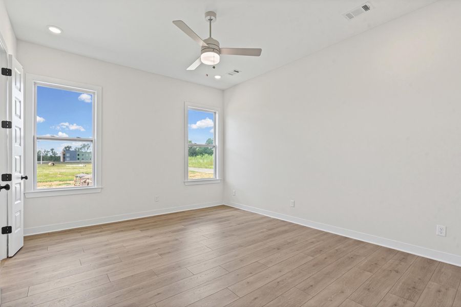 Light-filled room featuring two large windows with white trim, wood-finish flooring, recessed lighting, and a modern ceiling fan Light-filled room featuring two large windows with white trim, wood-finish flooring, recessed lighting, and a modern ceiling fan
