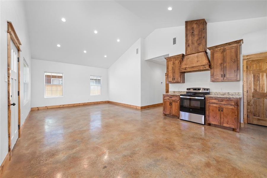 Kitchen featuring stainless steel range with electric stovetop, high vaulted ceiling, visible vents, baseboards, and brown cabinetry Kitchen featuring stainless steel range with electric stovetop, high vaulted ceiling, visible vents, baseboards, and brown cabinetry