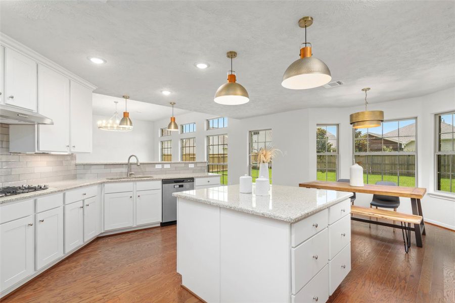 Stunning kitchen featuring granite countertops, white shaker cabinets, subway tile backsplash, stainless steel appliances, and a center island — all highlighted by designer gold and copper pendant lighting. Stunning kitchen featuring granite countertops, white shaker cabinets, subway tile backsplash, stainless steel appliances, and a center island — all highlighted by designer gold and copper pendant lighting.