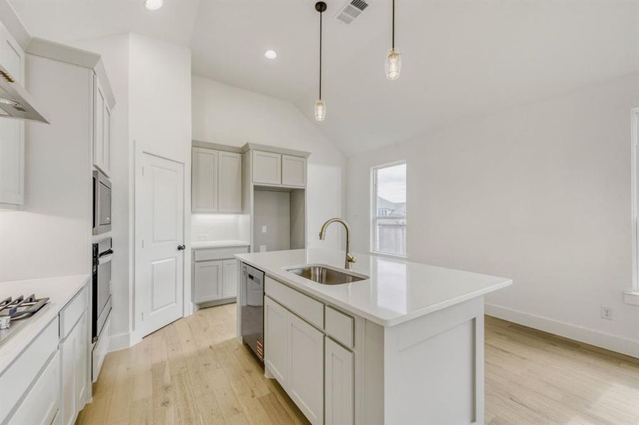 Kitchen featuring light wood-style floors, a center island with sink, vaulted ceiling, pendant lighting, and light stone countertops Kitchen featuring light wood-style floors, a center island with sink, vaulted ceiling, pendant lighting, and light stone countertops
