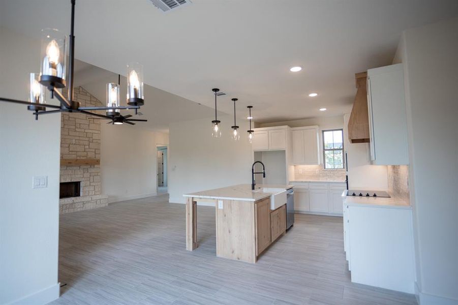 Kitchen featuring a breakfast bar, a center island with sink, a fireplace, white cabinetry, and light wood-style flooring Kitchen featuring a breakfast bar, a center island with sink, a fireplace, white cabinetry, and light wood-style flooring