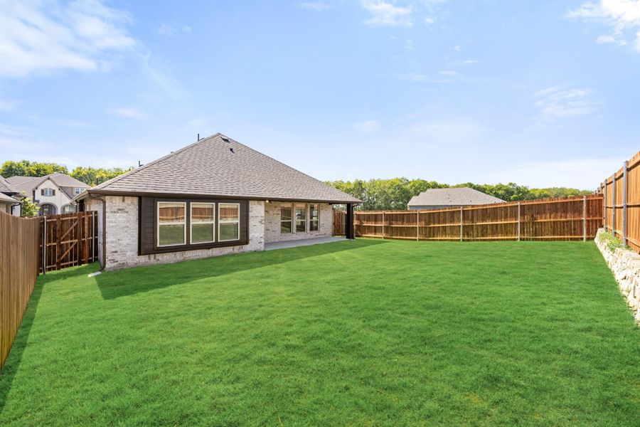 Backyard of brick home with large green lawn, wood privacy fence, and covered patio area