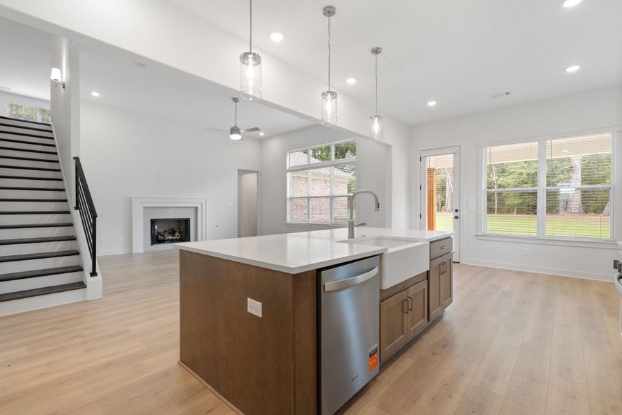 Kitchen island with a white farmhouse sink, stainless steel dishwasher, and pendant lighting Kitchen island with a white farmhouse sink, stainless steel dishwasher, and pendant lighting