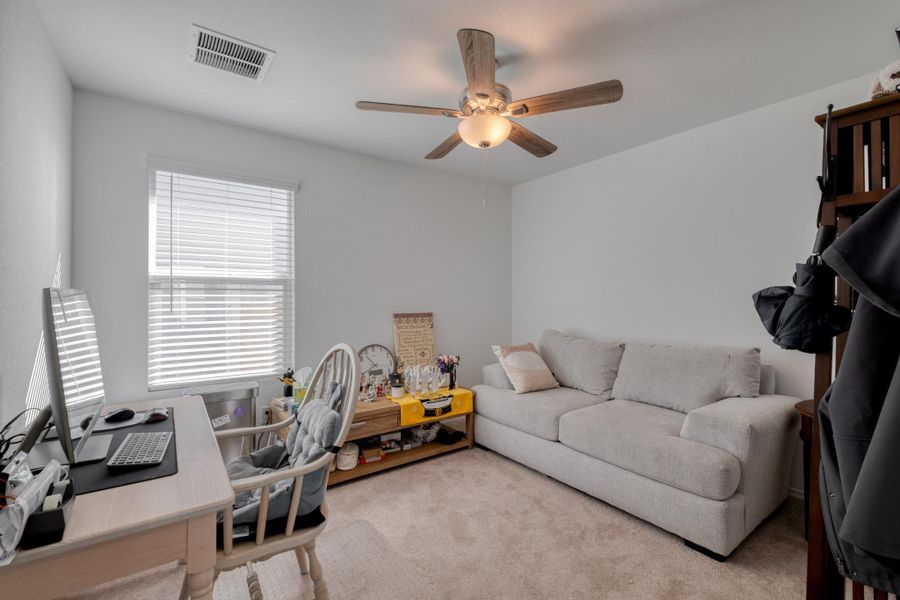 This versatile room features neutral carpeting, a ceiling fan with light fixture, and a window with blinds, providing natural light