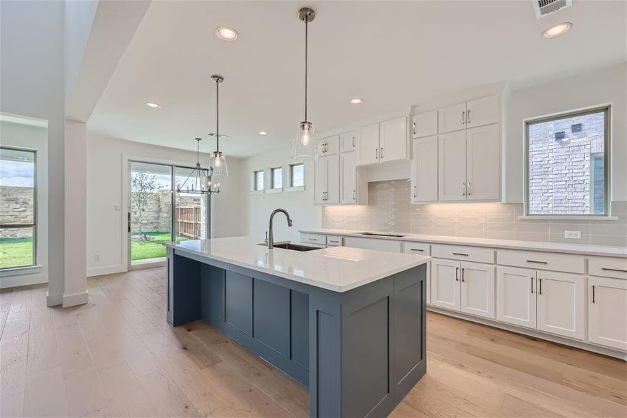 Kitchen featuring hanging light fixtures, a center island with sink, white cabinetry, light wood-type flooring, and sink