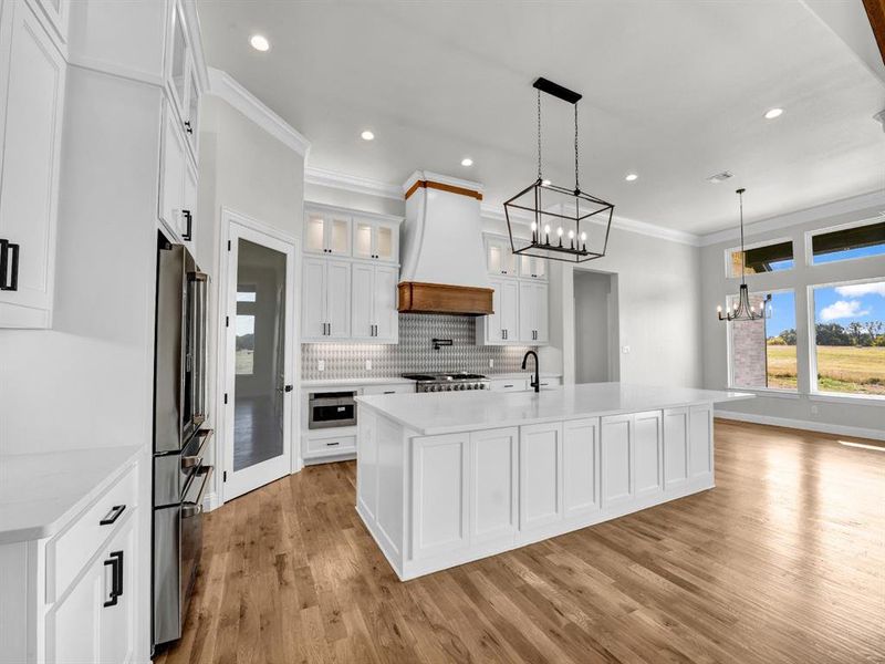 Kitchen featuring light wood-type flooring, hanging light fixtures, white cabinetry, stainless steel appliances, and a kitchen island with sink