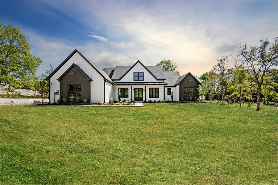 Modern inspired farmhouse featuring a standing seam roof, a front yard, a metal roof, and board and batten siding Modern inspired farmhouse featuring a standing seam roof, a front yard, a metal roof, and board and batten siding