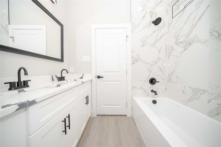 Bathroom with double vanity, a combined bath / shower with marble appearance, and light wood finished floors Bathroom with double vanity, a combined bath / shower with marble appearance, and light wood finished floors