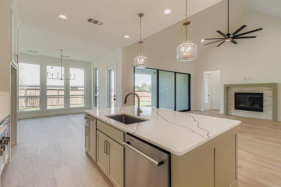 Kitchen with open floor plan, hanging light fixtures, stainless steel dishwasher, an island with sink, and light wood-style floors Kitchen with open floor plan, hanging light fixtures, stainless steel dishwasher, an island with sink, and light wood-style floors