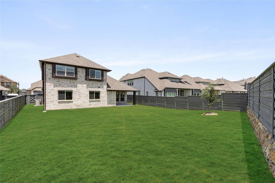 Backyard of two-story brick home with large green lawn and wood privacy fence Backyard of two-story brick home with large green lawn and wood privacy fence