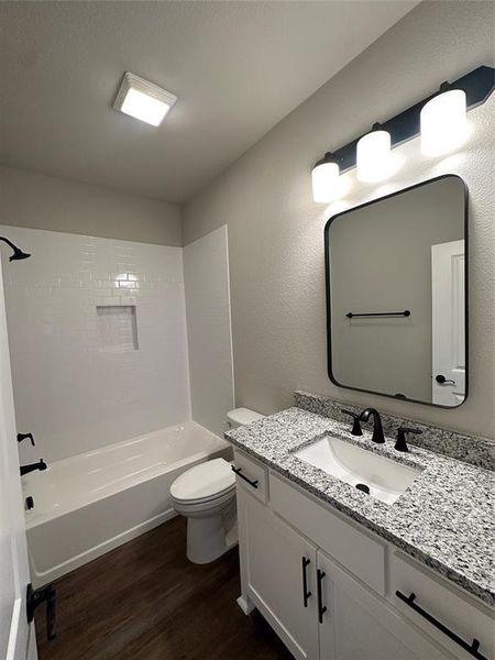 Full bathroom with vanity, hardwood / wood-style floors, tiled shower / bath combo, and toilet