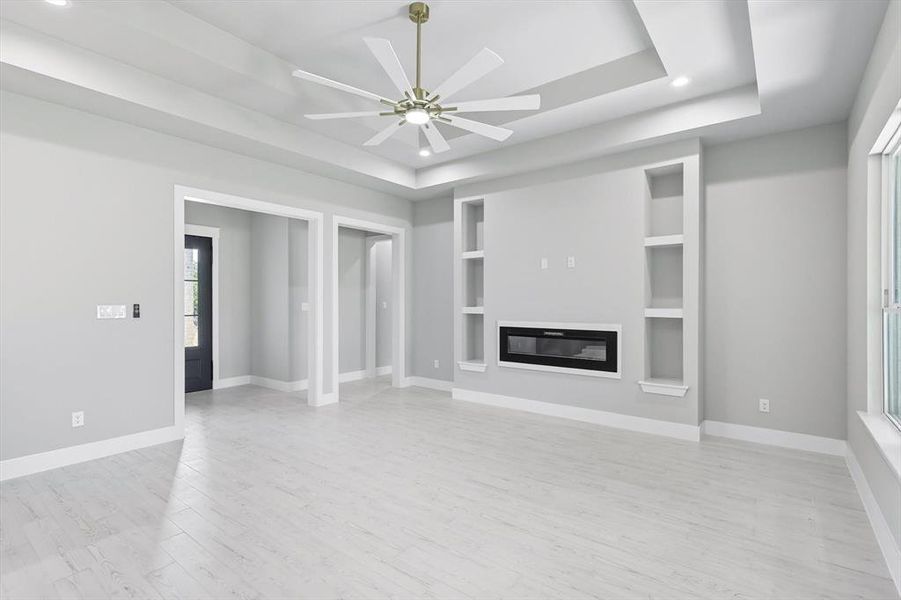 Unfurnished living room with a tray ceiling, light wood-style floors, a glass covered fireplace, ceiling fan, and recessed lighting
