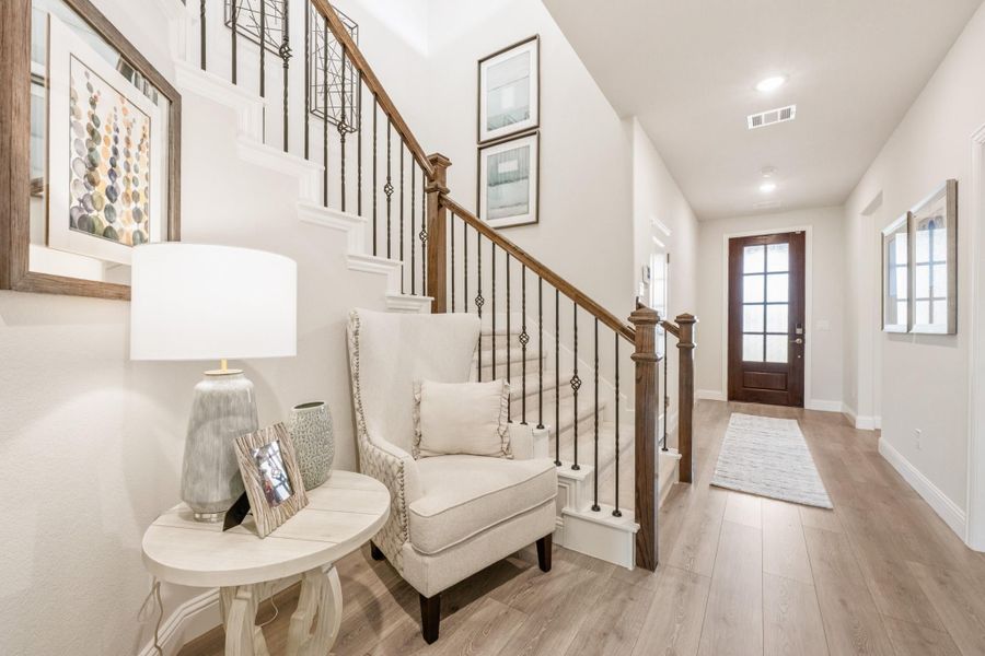 Bright home entryway with wood and iron staircase, hardwood floors, and accent chair near front door. Bright home entryway with wood and iron staircase, hardwood floors, and accent chair near front door.