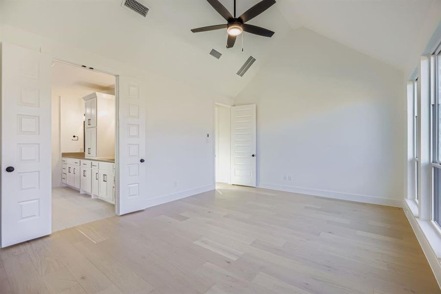 Unfurnished bedroom featuring light wood-type flooring, high vaulted ceiling, a ceiling fan, and ensuite bath