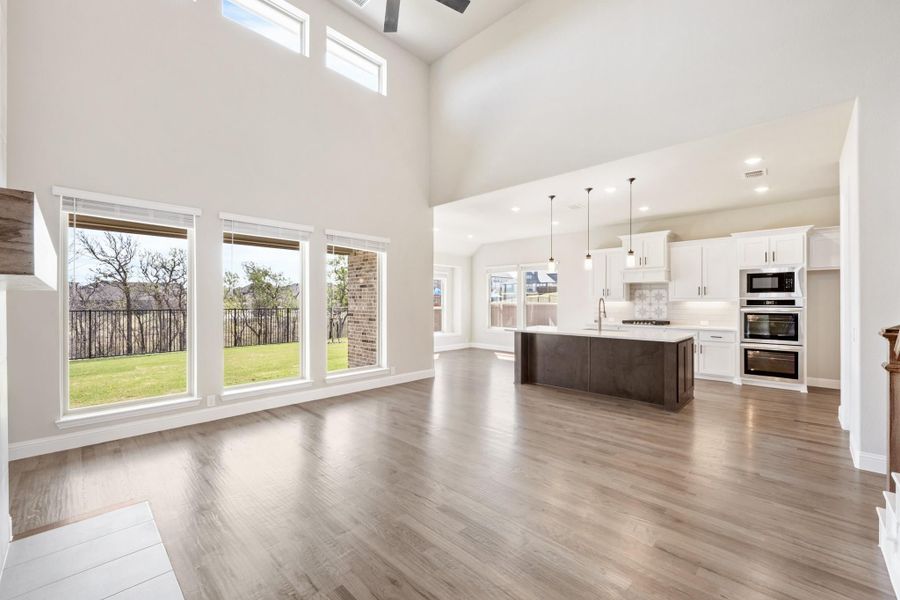 Open-concept living area with high ceilings and hardwood floors flowing into kitchen with dark island and white cabinets