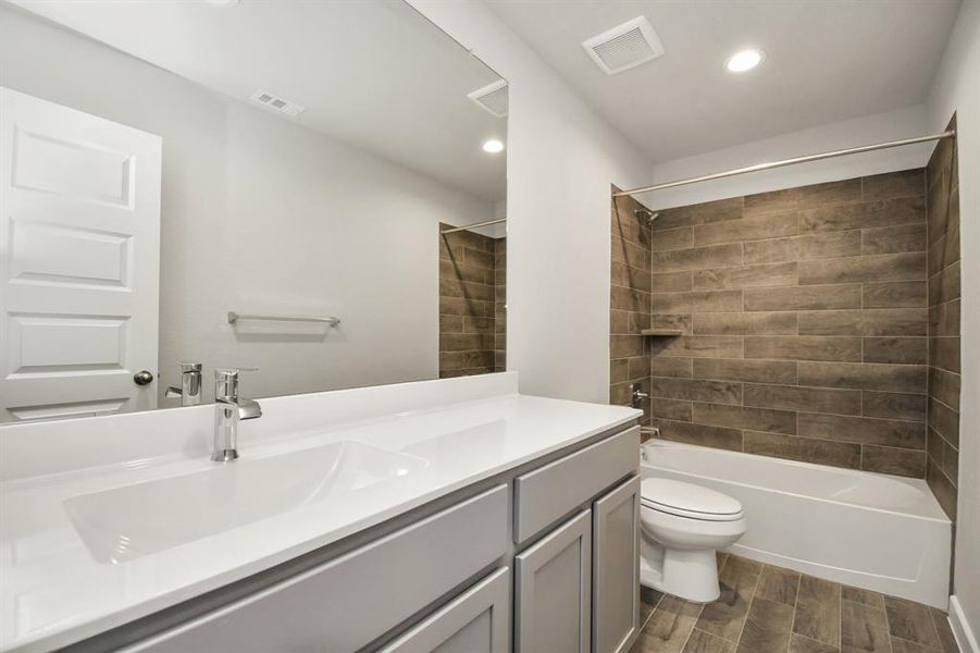 The secondary bath boasts stylish tile flooring, a bath/shower combo with a sleek tile surround, light colored cabinets, and a stunning light countertop.