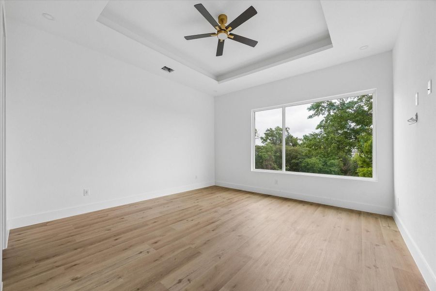 Primary suite showcasing a tray ceiling, ceiling fan, two walk-in closets, and an expansive picture window.