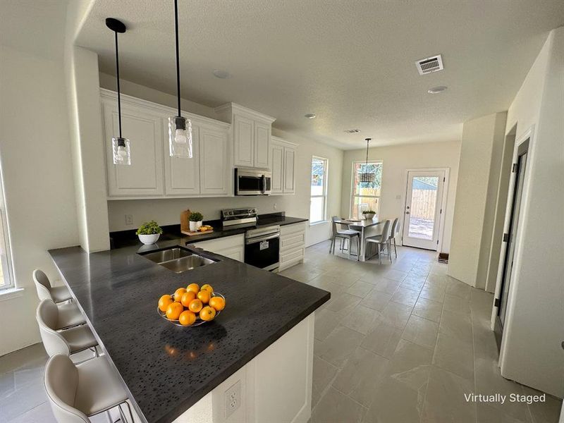 Kitchen featuring kitchen peninsula, white cabinetry, sink, decorative light fixtures, and stainless steel appliances