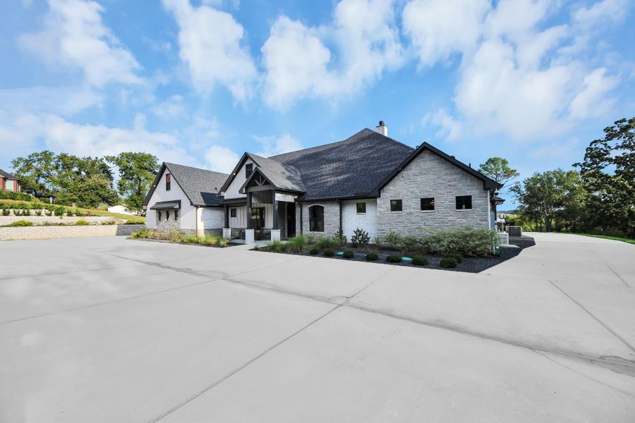Stunning modern home with a sleek stone exterior, expansive driveway, and beautifully landscaped surroundings, offering both elegance and privacy.