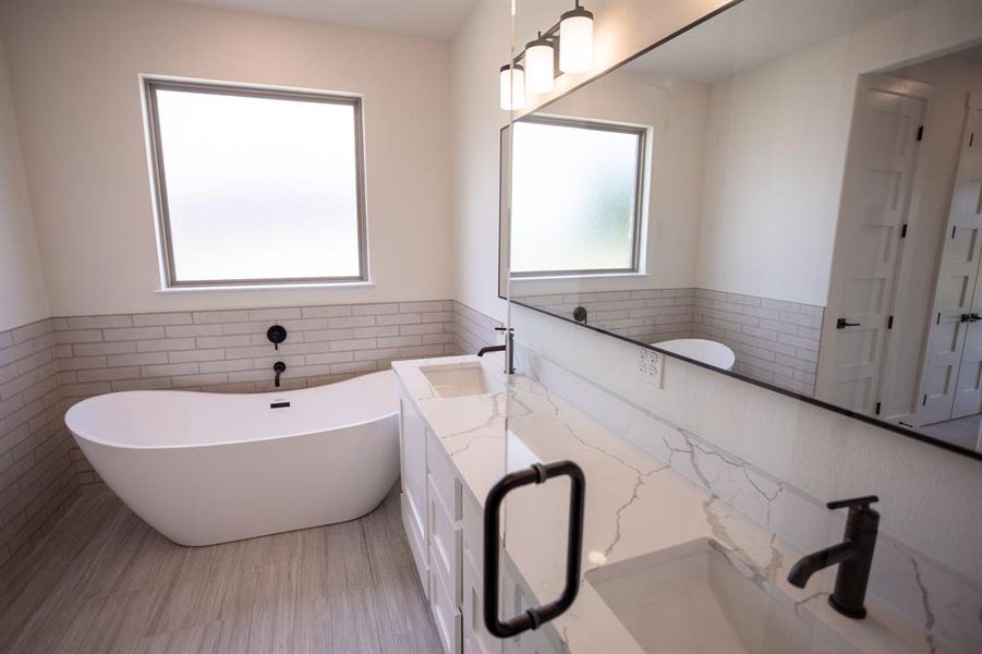 Full bath with tile walls, a soaking tub, a wainscoted wall, and double vanity Full bath with tile walls, a soaking tub, a wainscoted wall, and double vanity