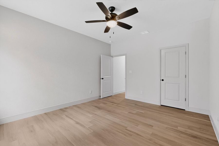 A well-proportioned bedroom with rich wood flooring, crisp walls, and a modern ceiling fan. A well-proportioned bedroom with rich wood flooring, crisp walls, and a modern ceiling fan.