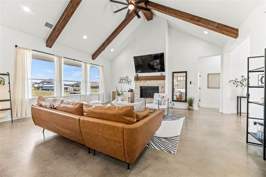 Living room with beam ceiling, high vaulted ceiling, a stone fireplace, finished concrete flooring, and a ceiling fan Living room with beam ceiling, high vaulted ceiling, a stone fireplace, finished concrete flooring, and a ceiling fan