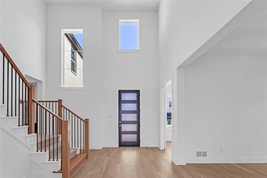 Entryway with light wood-style flooring, a towering ceiling, and stairs