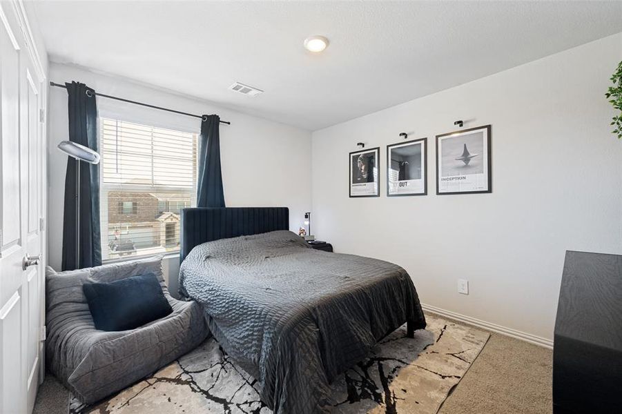 Bedroom featuring a large window with blinds and dark curtains, a gray textured area rug, and neutral wall tones Bedroom featuring a large window with blinds and dark curtains, a gray textured area rug, and neutral wall tones