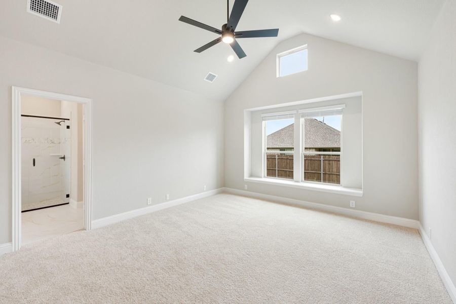 Spacious bedroom with vaulted ceiling, ceiling fan, carpet flooring, and ensuite bathroom entrance