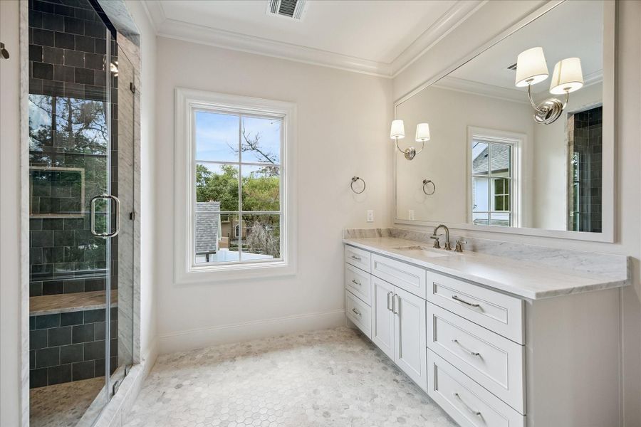 Well-appointed full bath in the mother-in-law/guest suite featuring a marble slab countertop and backsplash, custom vanity with polished hardware, and a framed mirror with sconce lighting. A frameless glass-enclosed shower with beautiful tile surround to the ceiling adds a refined, spa-like touch.