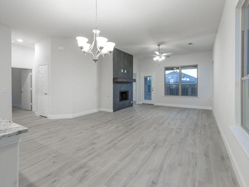 Unfurnished living room featuring a large fireplace, ceiling fan with notable chandelier, and light wood-type flooring