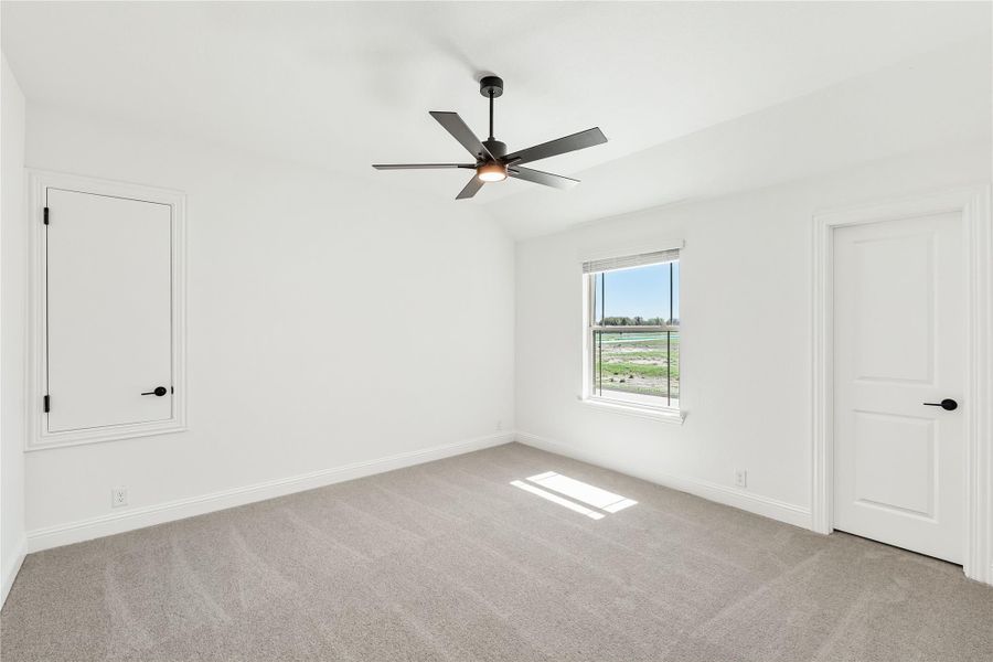 Empty bedroom with vaulted ceiling, ceiling fan, carpet flooring, and a window with outdoor views Empty bedroom with vaulted ceiling, ceiling fan, carpet flooring, and a window with outdoor views