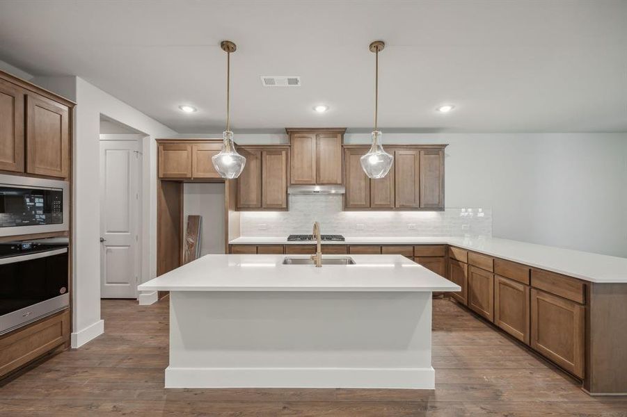 Kitchen with backsplash, decorative light fixtures, appliances with stainless steel finishes, and dark hardwood / wood-style flooring