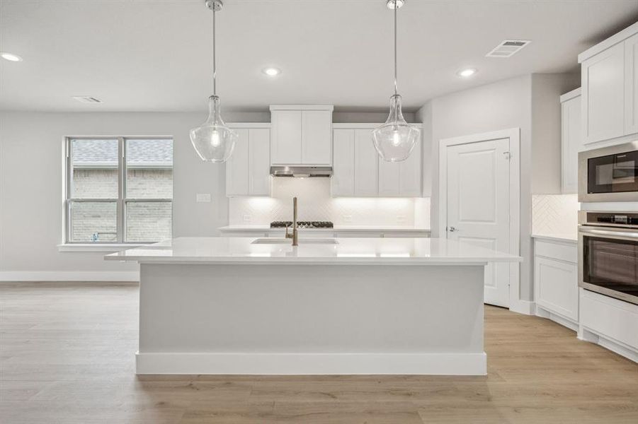 Kitchen featuring appliances with stainless steel finishes, pendant lighting, white cabinets, light wood-type flooring, and recessed lighting Kitchen featuring appliances with stainless steel finishes, pendant lighting, white cabinets, light wood-type flooring, and recessed lighting
