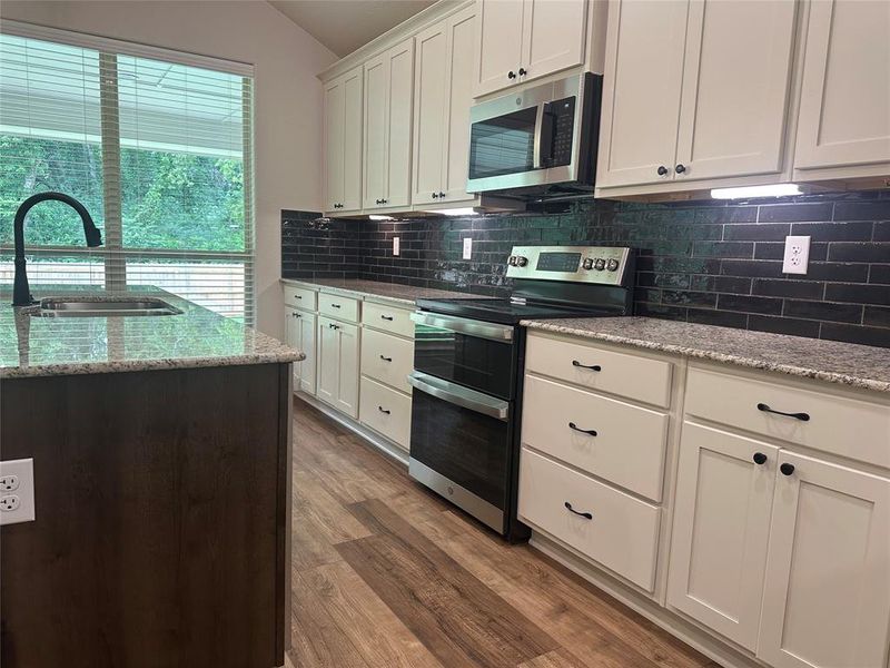 Kitchen featuring stainless steel appliances, lofted ceiling, decorative backsplash, light wood-style floors, and white cabinetry Kitchen featuring stainless steel appliances, lofted ceiling, decorative backsplash, light wood-style floors, and white cabinetry