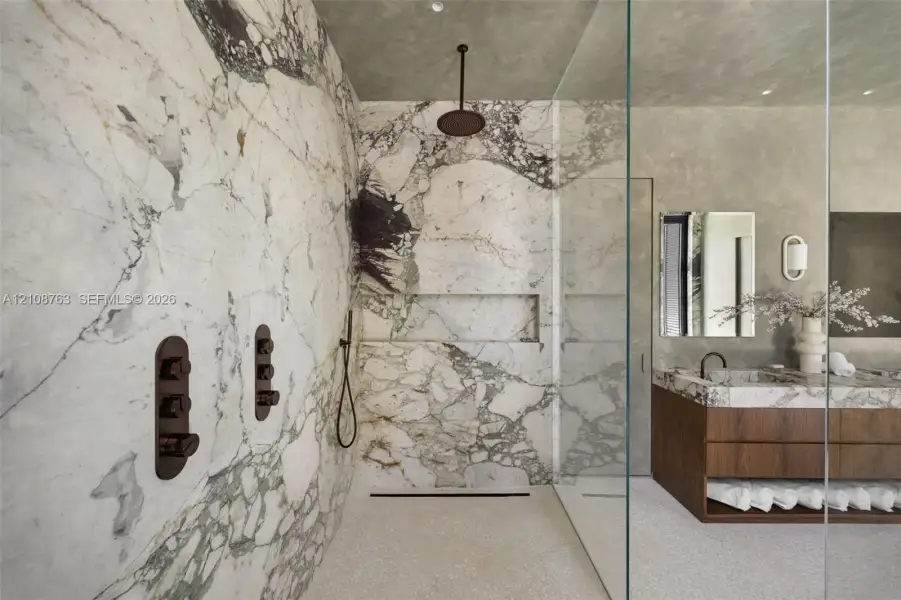 Walk-in shower with floor-to-ceiling stone slab wall surrounds, a built-in recessed niche, and matte black rain shower head and hardware